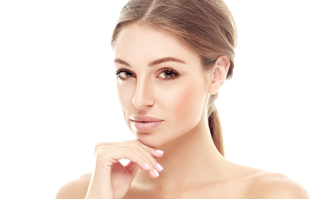 A person with brown hair is looking at the camera, resting their chin on their hand, against a white background.